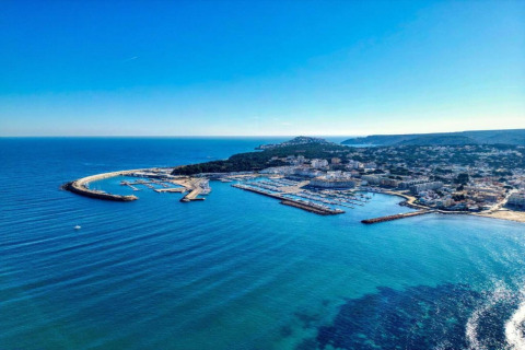 Aerial view of the marina and coastline at Nomad Paraiso in Spain, featuring clear blue water and buildings.