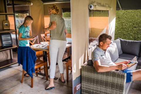 Een familie brengt tijd door in een safaritent, lezend op de sofa en activiteiten aan de tafel.