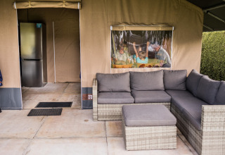 Tente safari avec canapé extérieur gris, réfrigérateur et famille réunie autour d’une table derrière la fenêtre.
