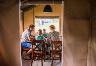 Une famille réunie autour d'une table dans une tente safari, partageant un moment convivial au camping.