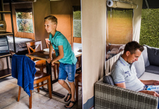 Garçon appuyé sur une table et homme lisant un magazine dans l’espace salon d’une tente safari.