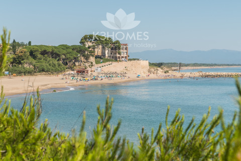View of the beach at Nomad Paraiso, Spain, featuring sandy shores, calm blue water, and lush greenery.