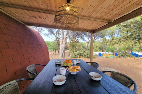 Outdoor breakfast on a wooden deck at Nomad Paraiso in Spain, overlooking trees and colorful tents.