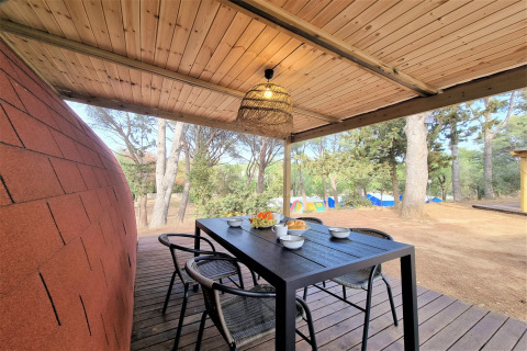 Covered patio at Nomad Paraiso pod in Spain, featuring a dining table, chairs, and views of forest and tents.
