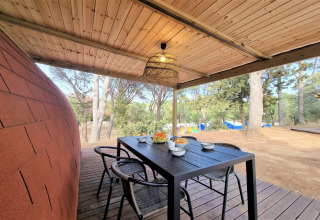 Covered patio at Nomad Paraiso pod in Spain, featuring a dining table, chairs, and views of forest and tents.