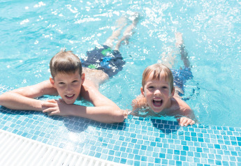 Zwei Kinder entspannen und lächeln am Beckenrand im Resort «Begur 1» in Spanien an einem sonnigen Tag.
