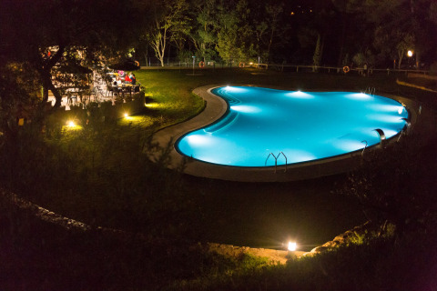 Verlichte buitenzwembad en tuinrestaurant bij nacht in Resort Begur 1 in Spanje, omringd door groen.