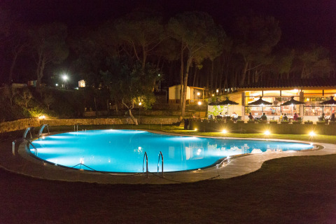 Verlicht zwembad ’s nachts bij Resort Begur 1 in Spanje met restaurant en gasten op de achtergrond.