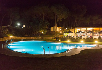 Beleuchtetes Schwimmbad bei Nacht im Resort Begur 1 in Spanien mit Restaurant und Gästen im Hintergrund.