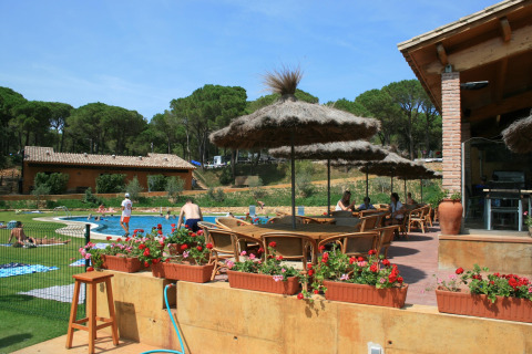 Buitenzwembadzone bij Resort «Begur 1» in Spanje, met mensen, parasols, bloemen en veel groen.