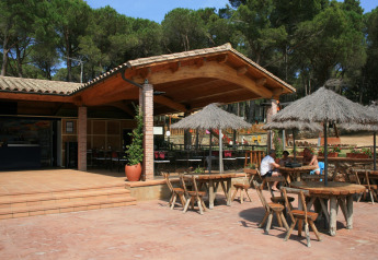Außenbereich mit Holztischen, Strohdachschirmen und Terrasse im Resort Begur 1 in Spanien.