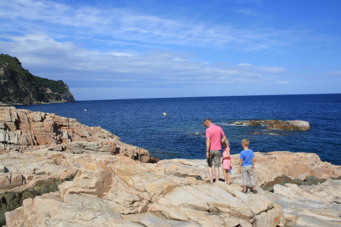 Een familie geniet van het uitzicht op zee vanaf de rotsen bij Resort «Begur 1» in Spanje onder een blauwe lucht.