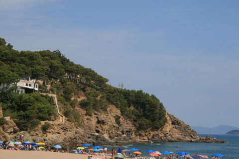 Zicht op een strand met kleurrijke parasols, rotsachtige kliffen en bomen bij Resort Begur 1 in Spanje.