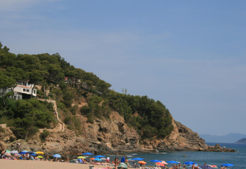 Strand mit bunten Sonnenschirmen, steilen Klippen und grünem Wald beim Resort Begur 1 in Spanien.