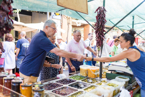 Bezoekers kopen verse olijven en fruit op een Spaanse markt, beschut door een grote markttent.