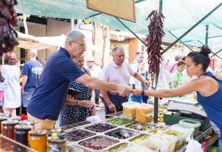 Bezoekers kopen verse olijven en fruit op een Spaanse markt, beschut door een grote markttent.