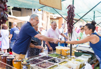 Menschen kaufen frisches Obst und Oliven auf einem lokalen Markt in Spanien unter einem schattigen Zelt.