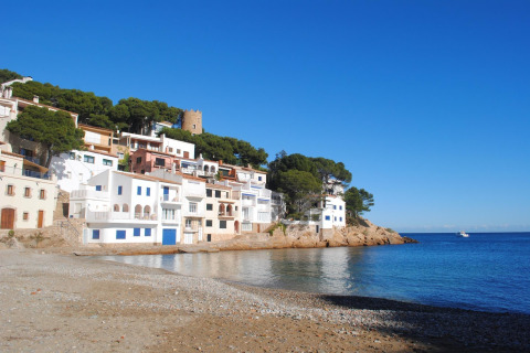 Zicht op witte kusthuizen in Begur, Spanje, bij de zee, onder een strakke blauwe lucht.