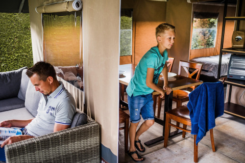 Homme lisant et garçon debout près de la table dans une tente safari confortable au Resort Begur 3 en Espagne.