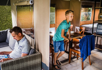 Homme lisant et garçon debout près de la table dans une tente safari confortable au Resort Begur 3 en Espagne.