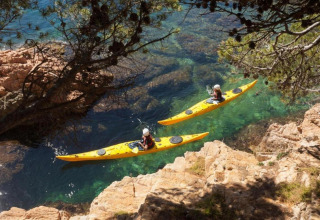 Deux personnes pagaient en kayak jaune sur une eau claire, entourées de rochers et de pins en Espagne.