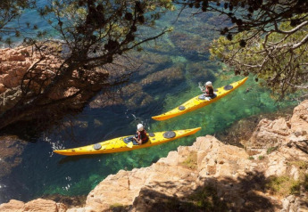 Deux personnes pagaient en kayak jaune sur une eau claire, entourées de rochers et de pins en Espagne.