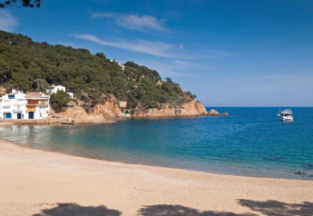 Belle plage au Resort Begur 3 en Espagne, avec falaises, pins, maisons blanches et un bateau sur la mer.