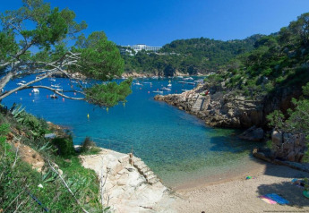 Superbe crique avec eau turquoise, plage de sable, collines verdoyantes et bateaux sous un ciel bleu.