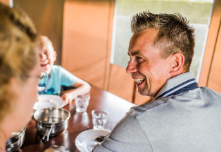 Un homme sourit et partage un repas avec sa famille à une table dans l’ambiance d’une tente safari.