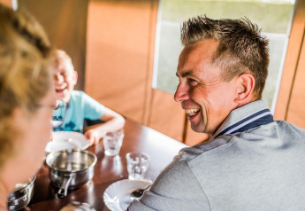 Un homme sourit et partage un repas avec sa famille à une table dans l’ambiance d’une tente safari.