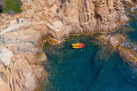 Aerial photo of kayaks in clear blue water by rocky cliffs at Resort «Begur 3» in Spain.