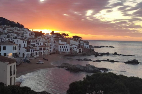 Beautiful sunset over a coastal village with white houses, sandy beach, boats, and calm sea.