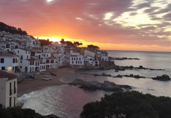 Superbe coucher de soleil sur un village côtier aux maisons blanches, plage de sable et mer calme.