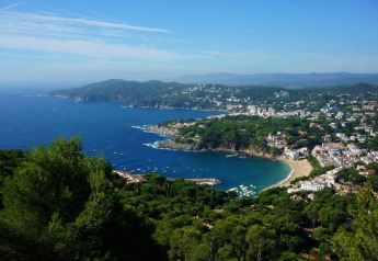Vue panoramique depuis Resort Begur 3 en Espagne, montrant la côte, la plage et la ville entourée d’arbres.