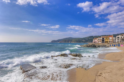 Strand- en zeezicht bij Resort «Begur 4» in Spanje met kleurrijke huizen aan de kust en rollende golven.