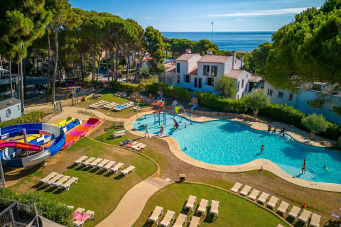 Camping Interpals Bungalow Sa Riera i Spanien med swimmingpool, vandrutsjebane og liggestole under træer.