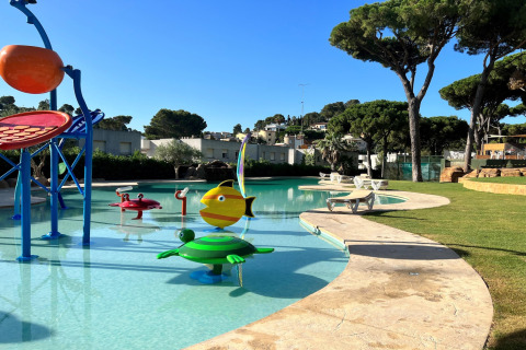 Udendørs børnepool med farverige vandlege ved CAMPING INTERPALS- Bungalow Sa Riera, Spanien, omgivet af grønne træer.
