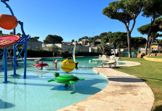Udendørs børnepool med farverige vandlege ved CAMPING INTERPALS- Bungalow Sa Riera, Spanien, omgivet af grønne træer.