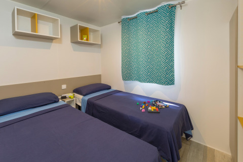 Værelse med to enkeltsenge med blåt sengetøj, legetøj på sengen og moderne indretning på Camping Interpals Bungalow Sa Riera i Spanien.