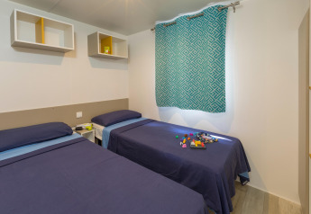 Kamer met twee eenpersoonsbedden, blauwe lakens, speelgoed en moderne inrichting in Camping Interpals Bungalow Sa Riera in Spanje.