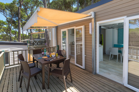 Udendørs terrasse med bord og stole på CAMPING INTERPALS- Bungalow Sa Riera, omgivet af fyrretræer.