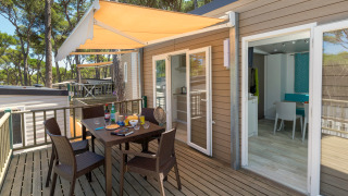Veranda esterna con tavolo e sedie al CAMPING INTERPALS- Bungalow Sa Riera, immersa tra pini.