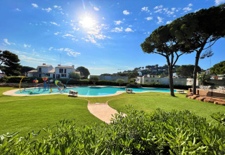 Solrig udsigt over poolområdet og grønne græsplæner på CAMPING INTERPALS- Bungalow Sa Riera i Spanien.