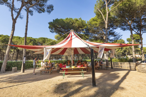 Børn og voksne sidder under et stort cirkustelt ved Camping Interpals - Bungalow Sa Riera i Spanien.