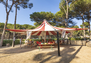 Børn og voksne sidder under et stort cirkustelt ved Camping Interpals - Bungalow Sa Riera i Spanien.