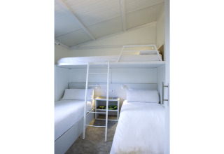 Lichte, moderne slaapkamer met stapelbedden en wit interieur in Tamarit Park Resort 1 THALASSA, Spanje.