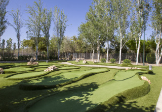 Miniature golfbane med grønne kunstgræsbaner, klipper og træer i Tamarit Park Resort, Spanien.