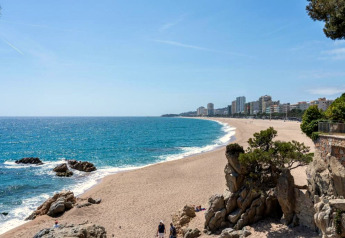 Vue de plage depuis Camping Interpals-Bungalow Sa Riera en Espagne, avec mer bleue, sable et immeubles en arrière-plan.