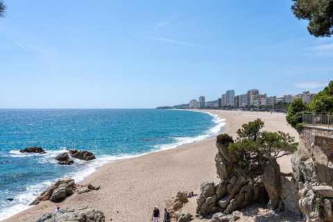 Smuk strandudsigt fra Camping Interpals-Bungalow Sa Riera i Spanien med klippeformationer og by i baggrunden.