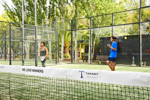 Deux personnes jouent au padel sur un terrain extérieur entouré d’arbres au Tamarit Beach Resort glamping.